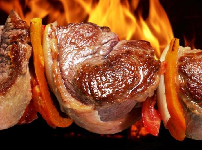 close de um espeto de churrasco com um belo pedaço de carne envolto numa chama.