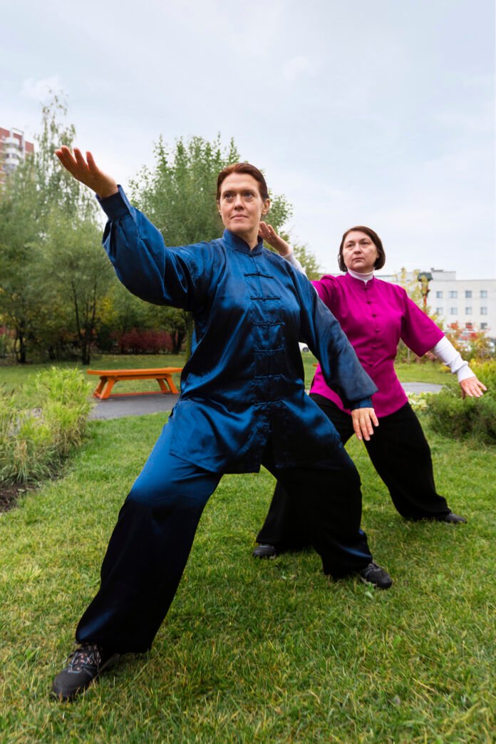 duas senhoras, uma de quimono de tai chi azul e outra de vermelho, praticando ao ar livre.