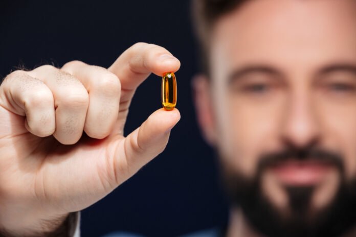 homem adulto exibindo capsula de omega-3 em primeiro plano.