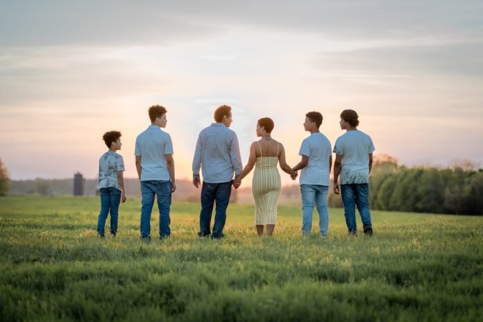 uma família de mãos dadas num campo ao por do sol, vistos de costa.
