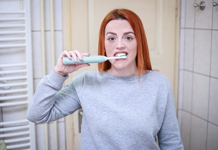 uma jovem escovando os dentes em frente ao espelho.