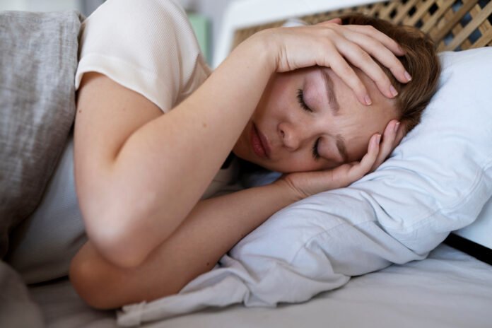 mulher deitada na cama com as mãos sobre os ouvidos.