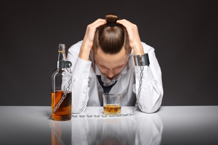 homem de cabeça baixa em frente a uma garrafa de whisky