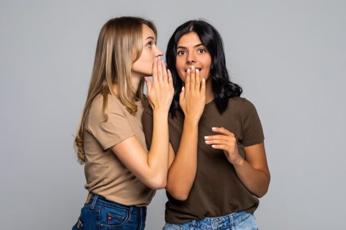 duas jovens mulheres conversando de forma discreta, cobrindo a boca com a mão.