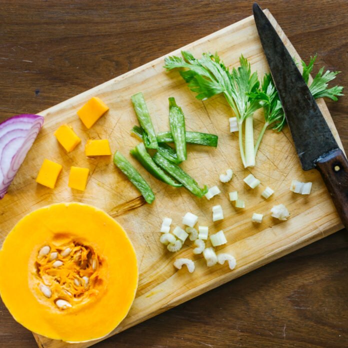 Diversos ingredientes vegetais em uma tabua de cozinha sendo cortados