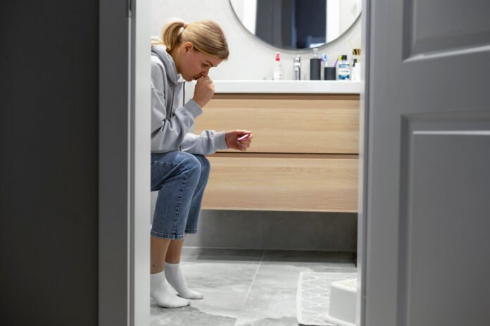 mulher de calça jeans, sentada no vazo sanitário sofrendo incontinência urinaria.