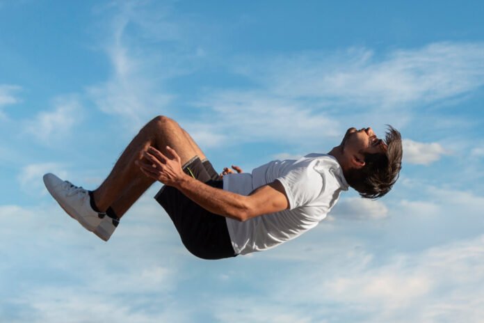 Um jovem de bermudas e tênis, em queda livre com o céu azul.