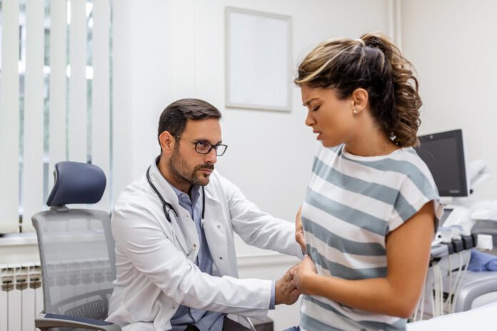 Um medico no seu consultório, examinando a região do fígado de uma paciente.