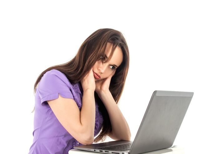 uma jovem sentada em frente a um notebook com as mãos apoiando o queixo .