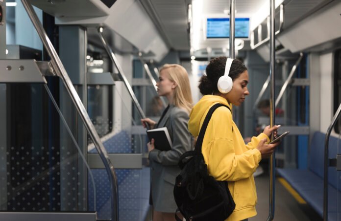 foto do interior de um vagão de metro, com uma jovem de moletom amarelo com headfones brancos em primeiro plano.