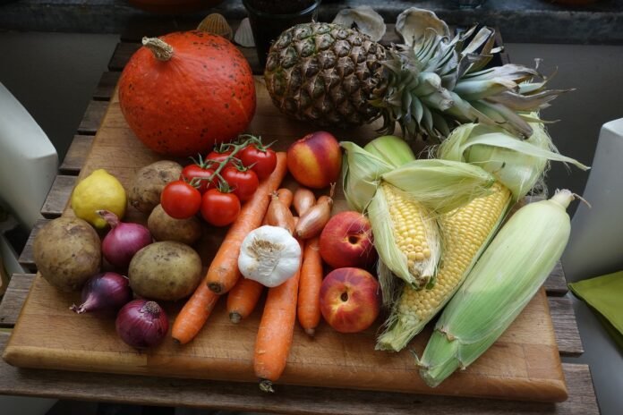 mesa com vários alimentos ricos em fibra como milho verde, abacaxi, cenoura, pêssego e tomates.