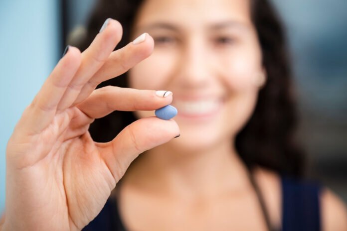 mulher mostrando uma pílula de Viagra em primeiro plano.