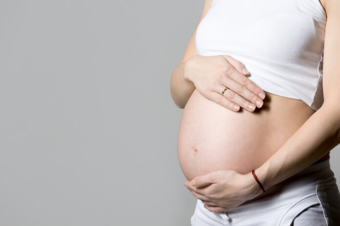 close de uma barriga em gravidez avançada, sendo acariciada pelas mãos.