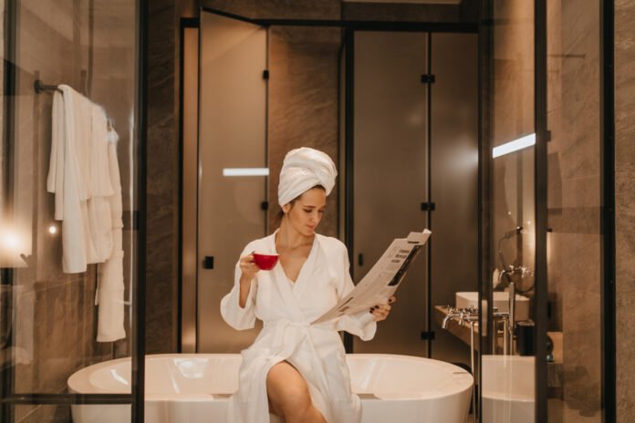uma jovem mulher sentada na orda de uma banheira lendo jornal.