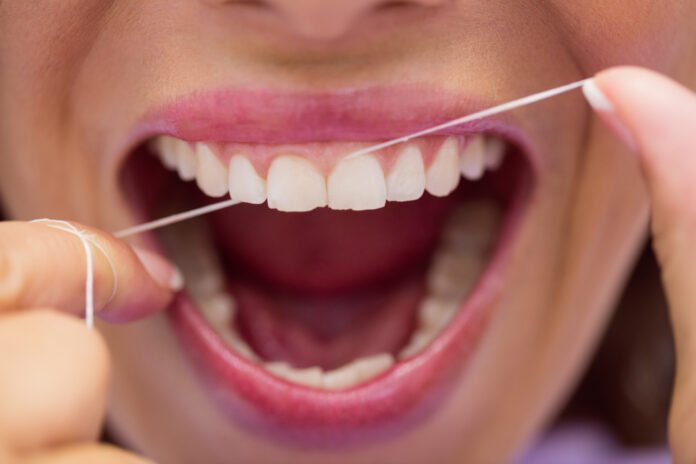 close de uma boca de uma jovem usando fio dental.